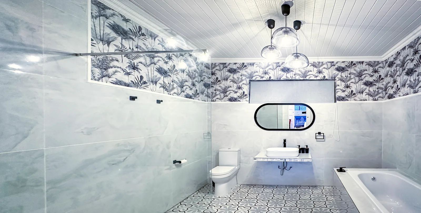Bathroom with marble-look tiles, botanical wallpaper, a walk-in glass shower, a basin with an oval mirror and a bath